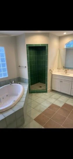 Bathroom with dark green shower tile and mixed-color flooring before resurfacing
