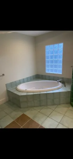Corner bathtub with green tile deck and mixed-color floor before resurfacing