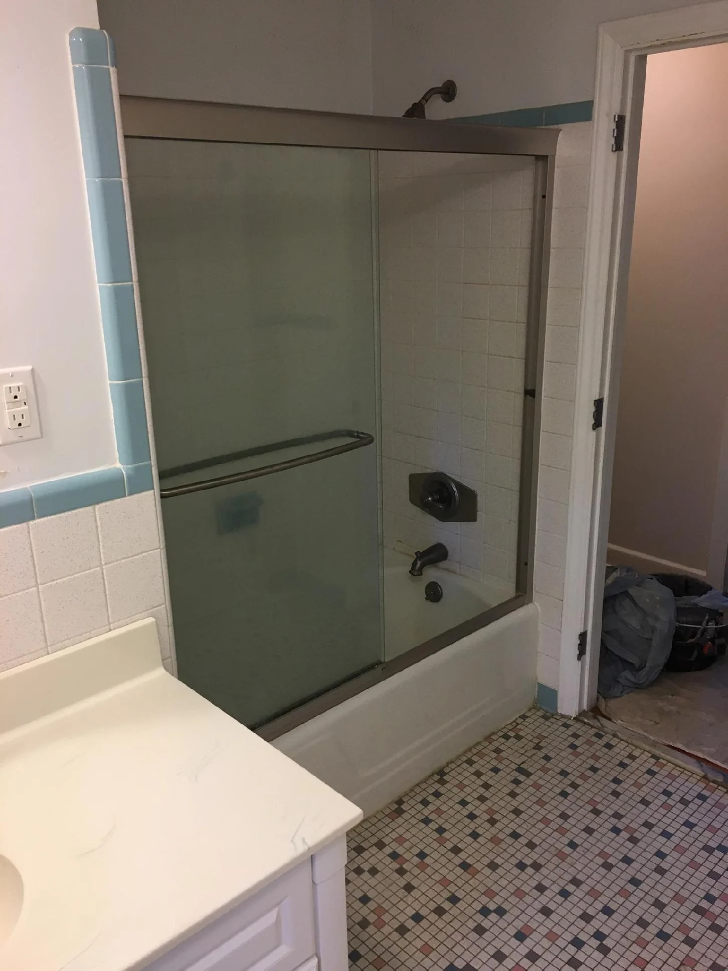 Dated bathtub, shower door, tile, and bathroom floor before refinishing